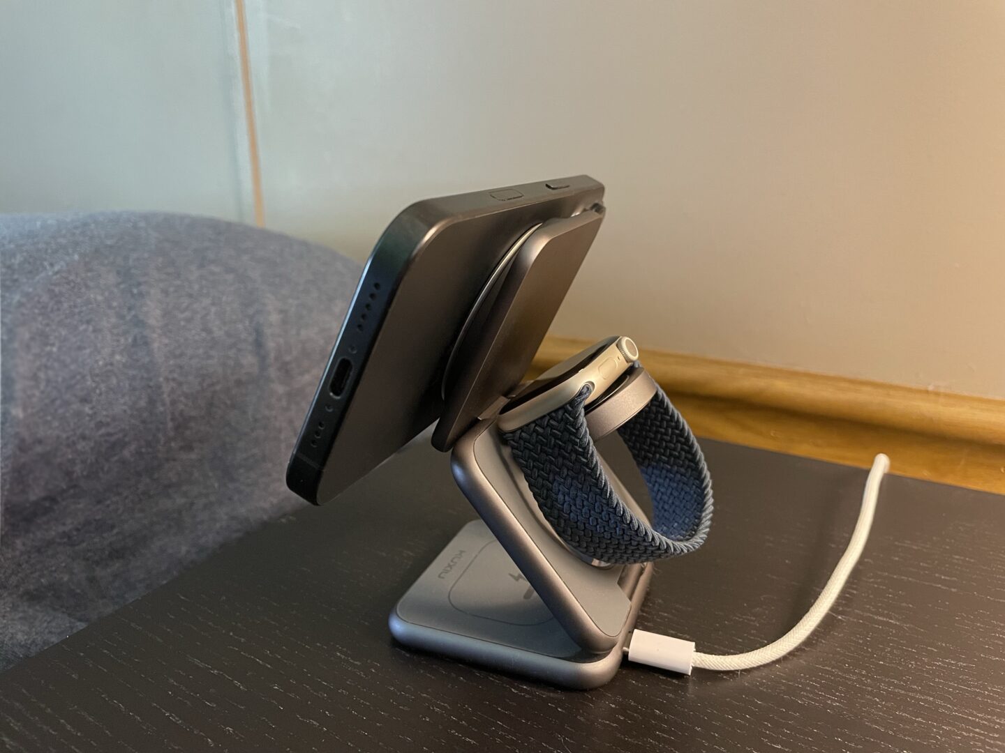 Photo of a black iPhone 16 Pro sitting on a nightstand attached to a MagSafe charger with the Ohsnap Snap 4 Luxe.