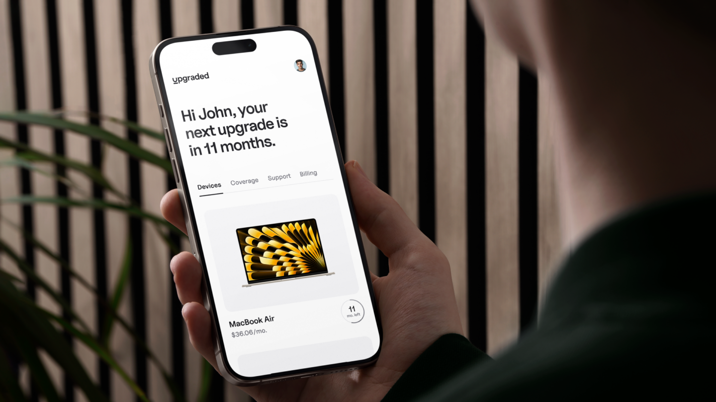 Photo of a person holding an iPhone with the Upgraded app on its screen, showing the words, "Hi John, your next upgrade is in 11 months."